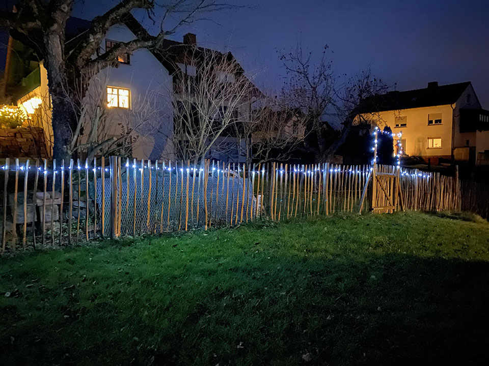 Staketenzaun mit Tor und Lichterkette bei Nacht